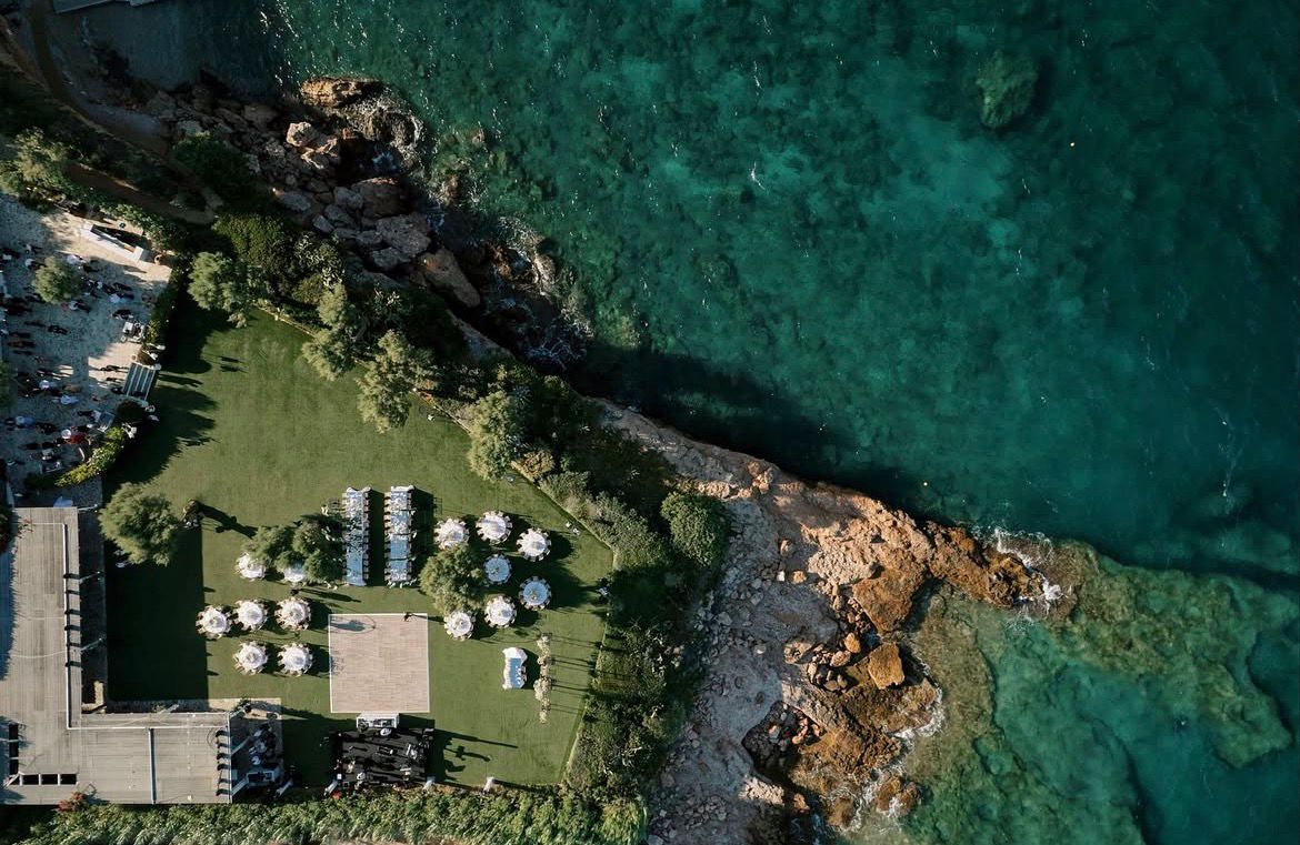 Aerial view of the Island Athens Riviera reception lawn beside turquoise sea
