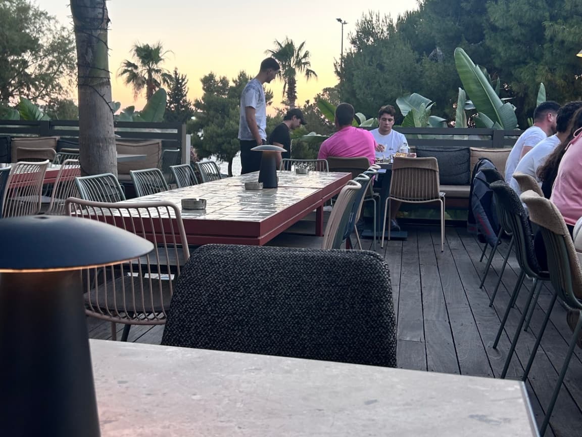 Long communal tables and woven chairs on the Rumors terrace at sunset