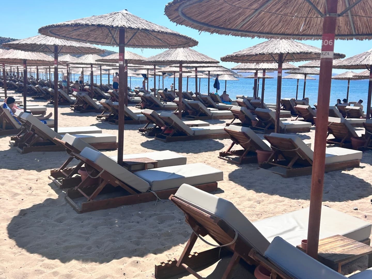 Sunbeds and woven umbrellas on a sandy beach at a Greek beach club